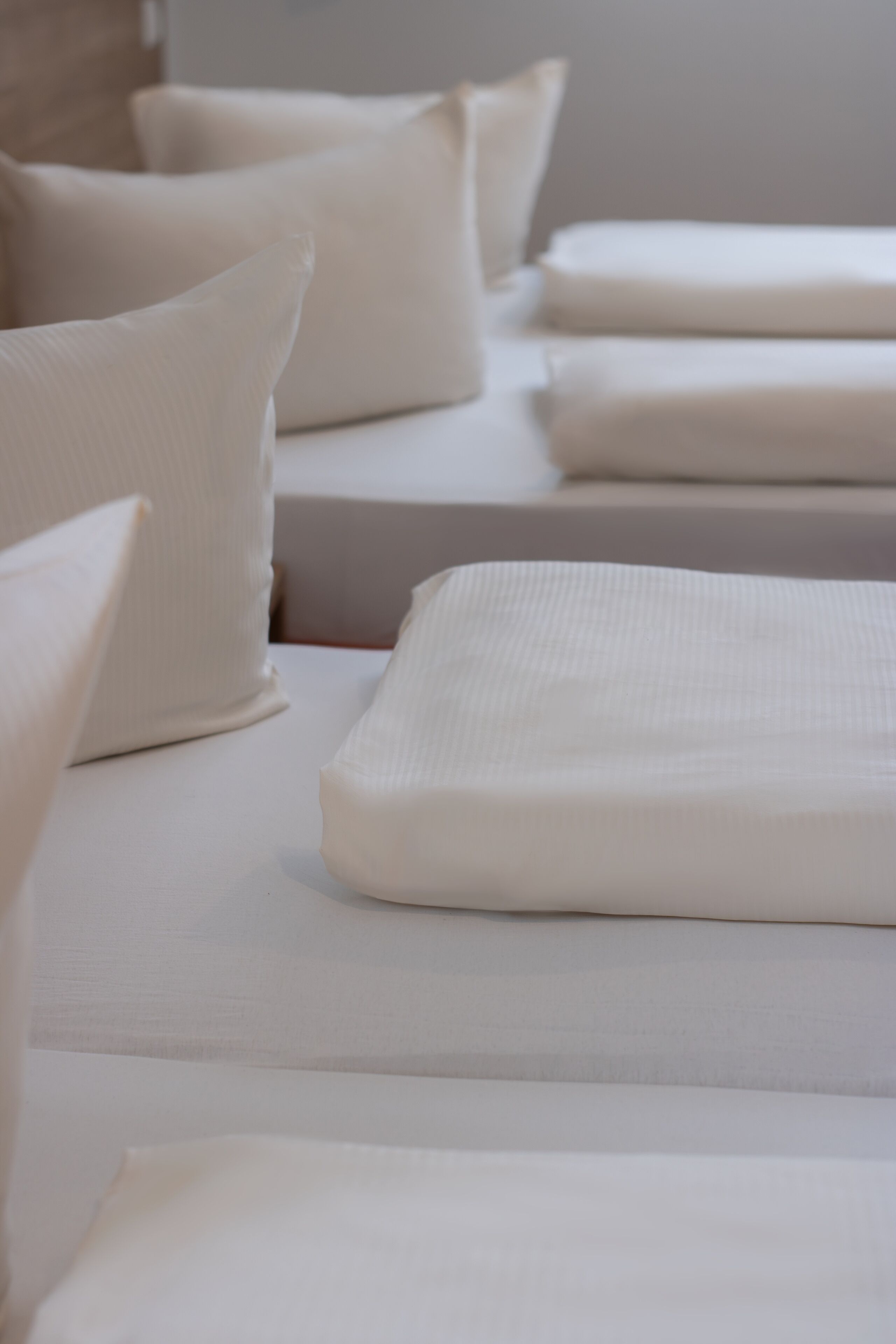 Varias camas ordenadas con sábanas blancas y almohadas, sugiriendo una habitación de hotel limpia y organizada.