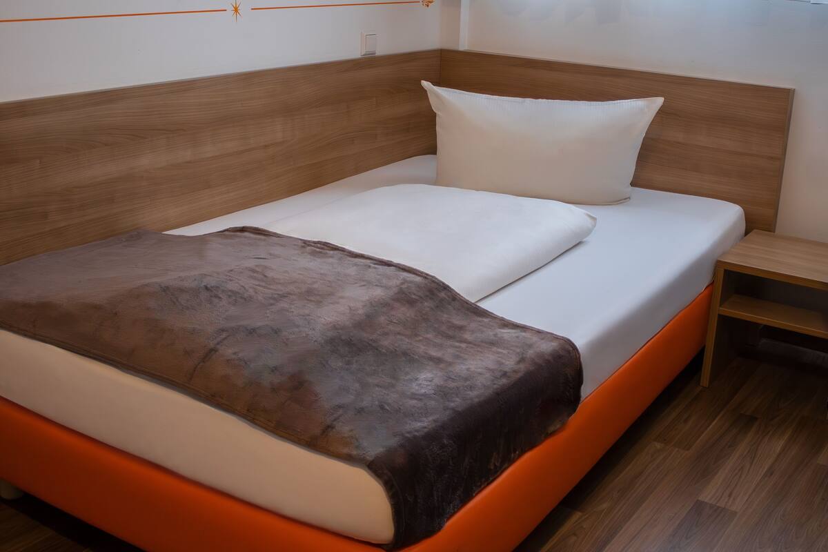 A bed with a wooden headboard, white bedding, and an orange accent.