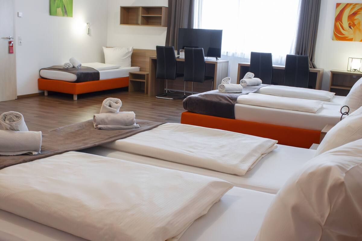 A hotel room with multiple beds, a desk, and a TV.