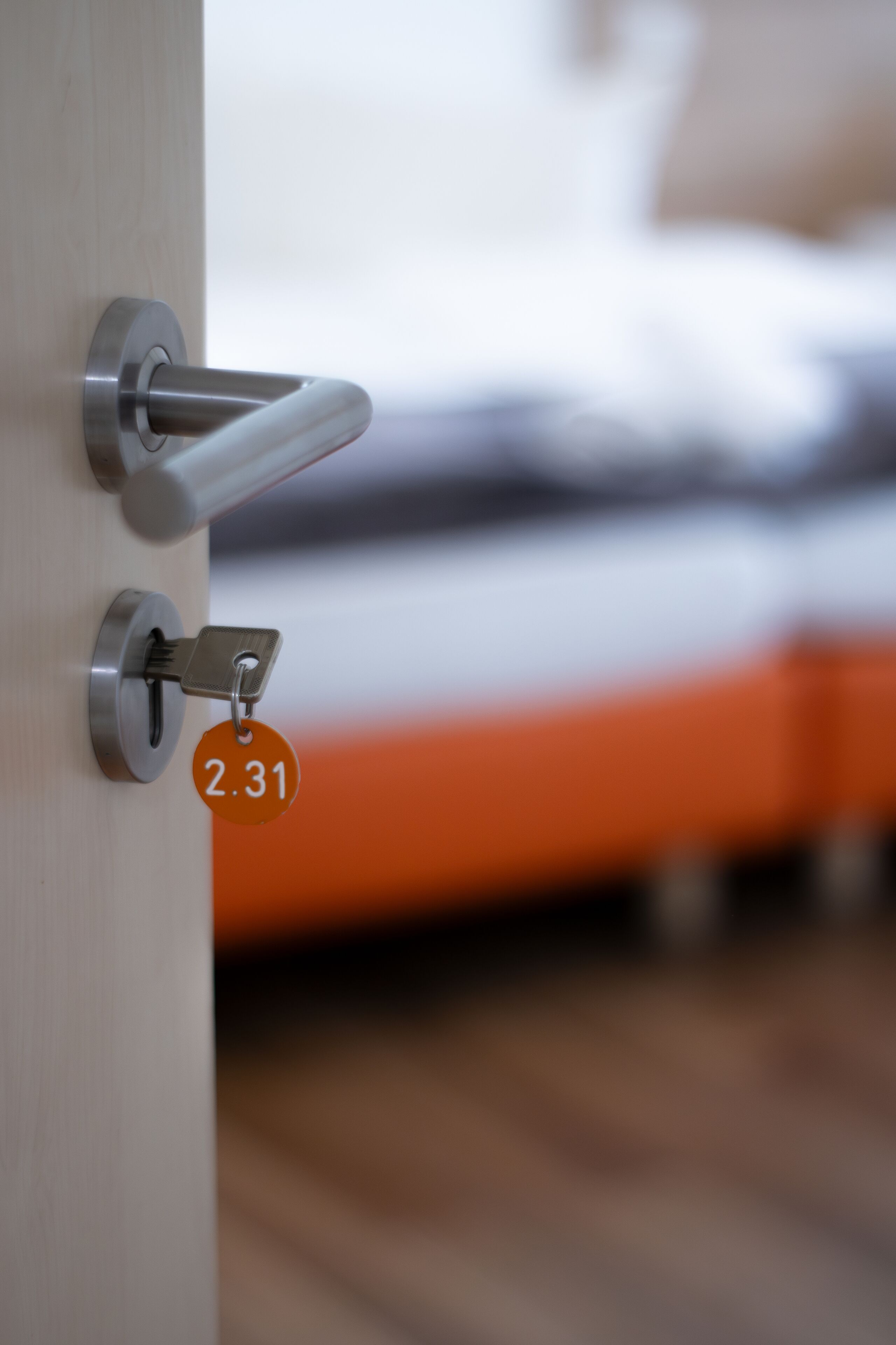 A door with a keyhole and a lock, a bed with an orange bedspread, and a wooden floor.