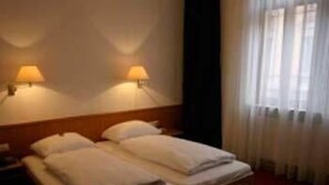 A hotel room with a double bed, two bedside lamps, and a window with curtains. - Krokodil Restaurant & Hotel (Heidelberg)