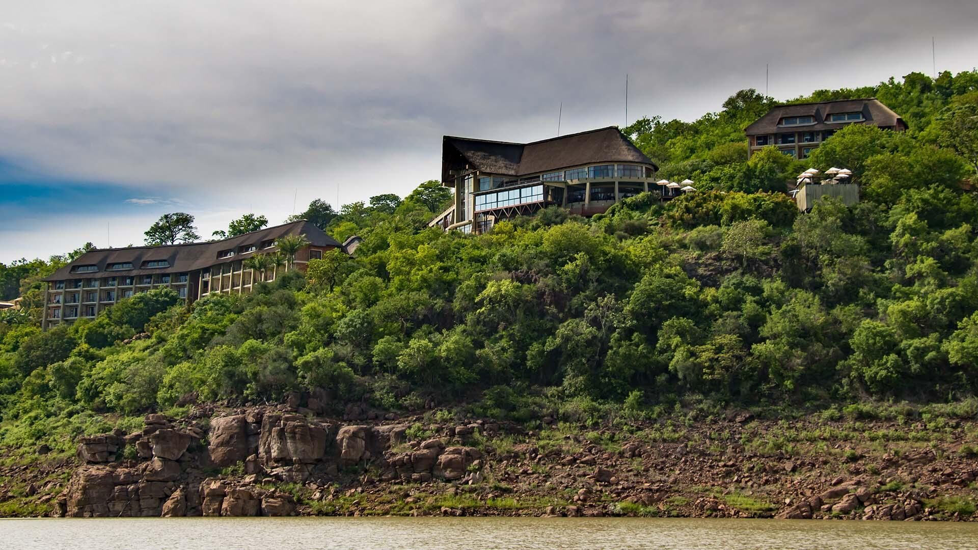 Un hotel con varias construcciones, una costa rocosa y abundante vegetación.