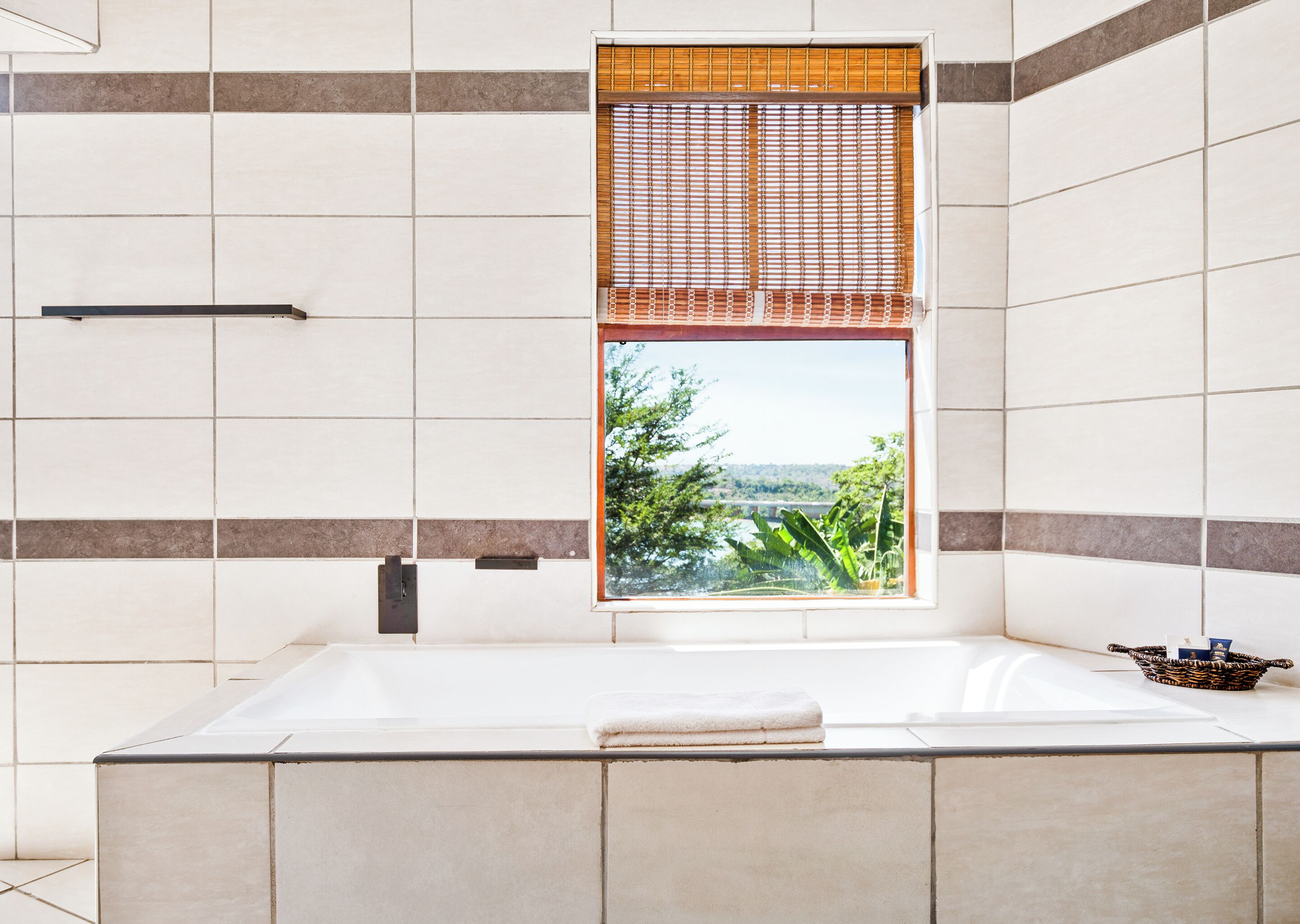 Un baño moderno con una bañera grande, una ventana que ofrece vistas a zonas verdes y una toalla en el borde.