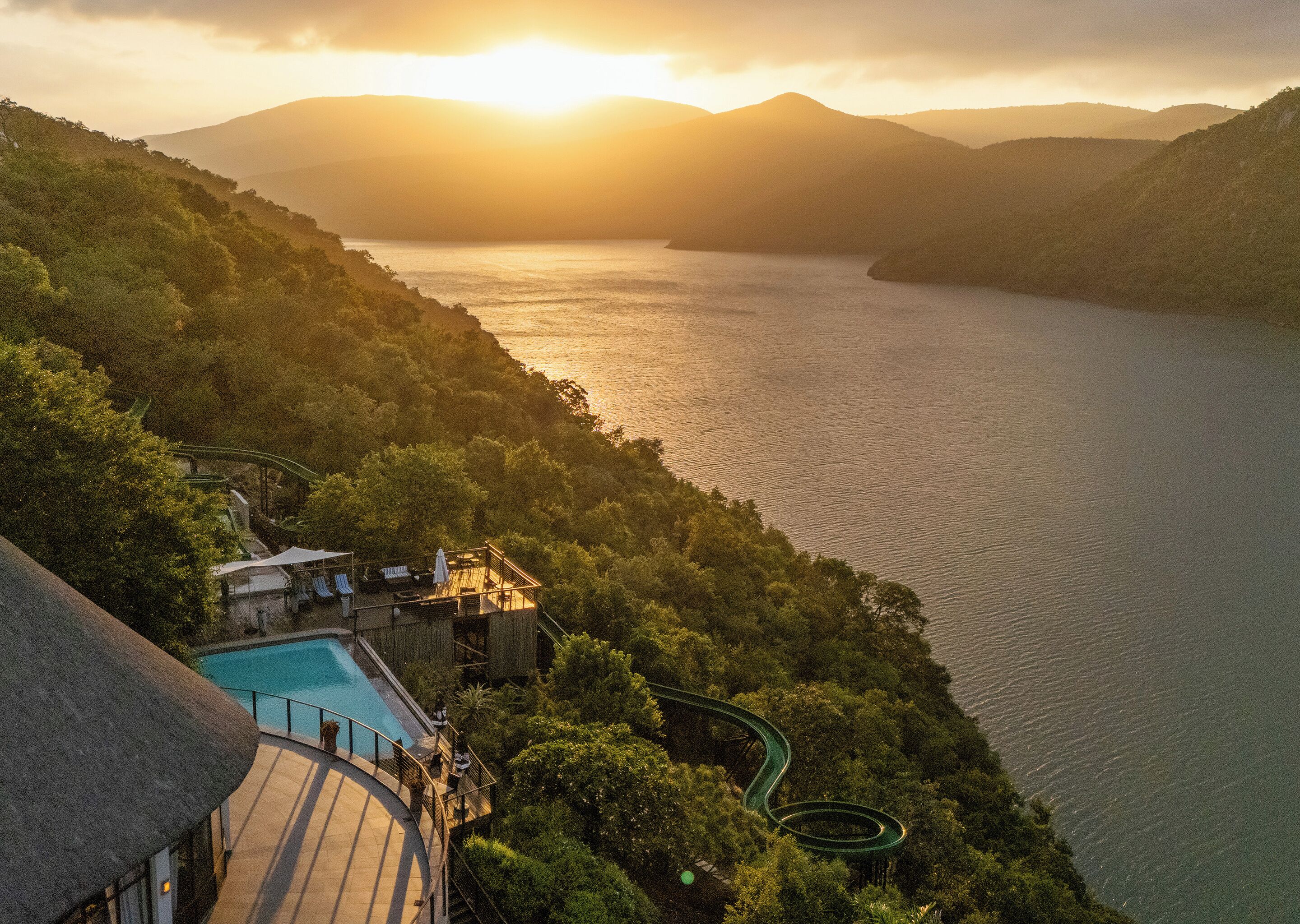 Un complejo turístico con piscina, rodeado de exuberante vegetación y vistas a una amplia extensión de agua.