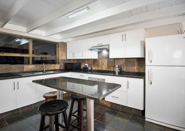 A modern kitchen with white cabinets, a granite countertop, and a stainless steel refrigerator.