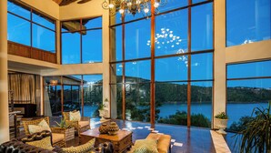 A spacious living area with large windows, leather sofas, and a view of a lake. - Jozini Tiger Lodge by Dream Resorts (Jozini)