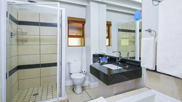 Ein modernes Badezimmer mit einer Glasdusche, einer Toilette, einem Waschbecken mit Spiegel und einer Badewanne.