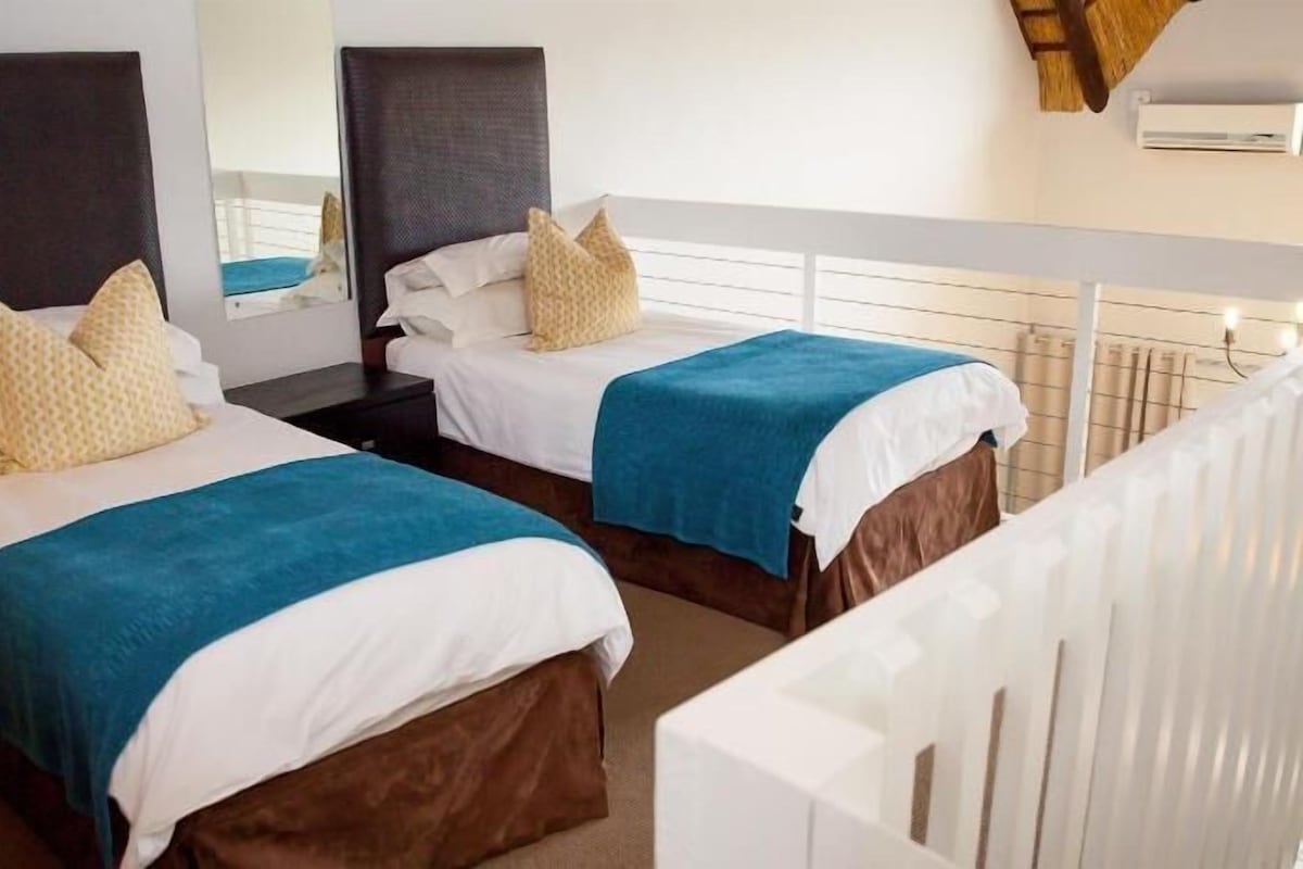 Dos camas individuales con cabeceros, ropa de cama blanca y mantas azules.
