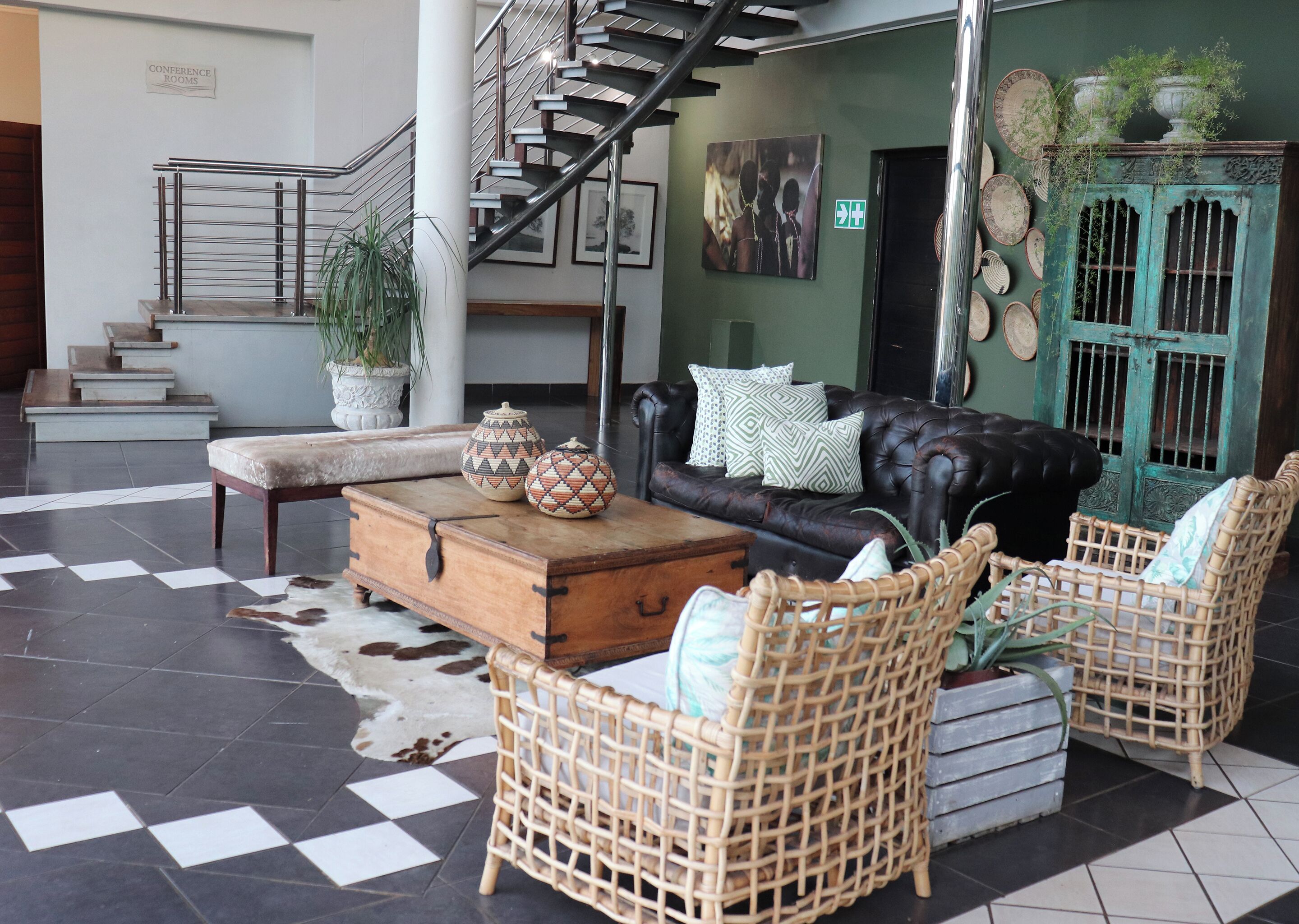 A lobby with a staircase, a leather sofa, wicker chairs, a wooden coffee table, and decorative pottery.