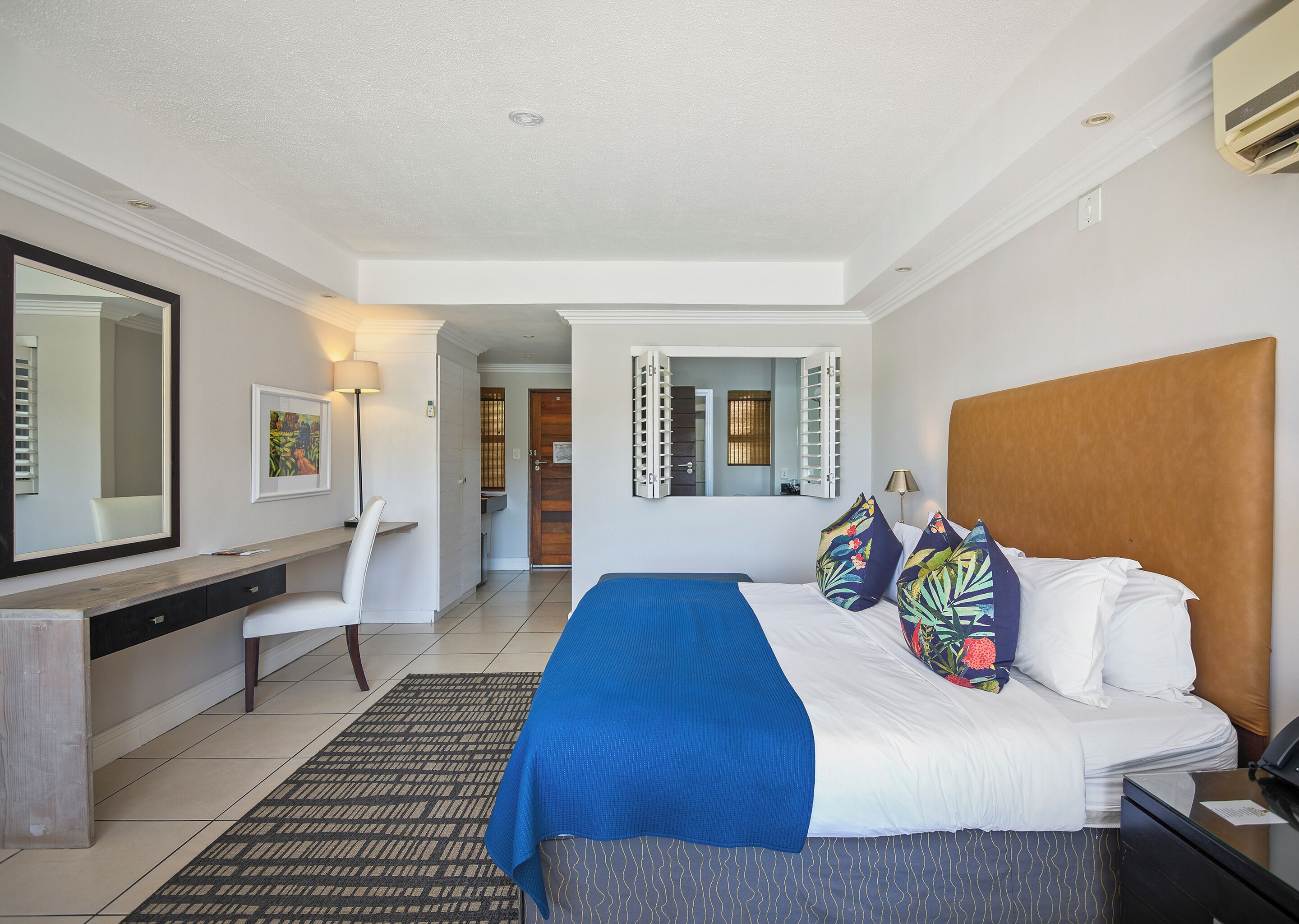 Une chambre d’hôtel comprenant un lit, une table de chevet, un bureau, une chaise et un grand miroir.
