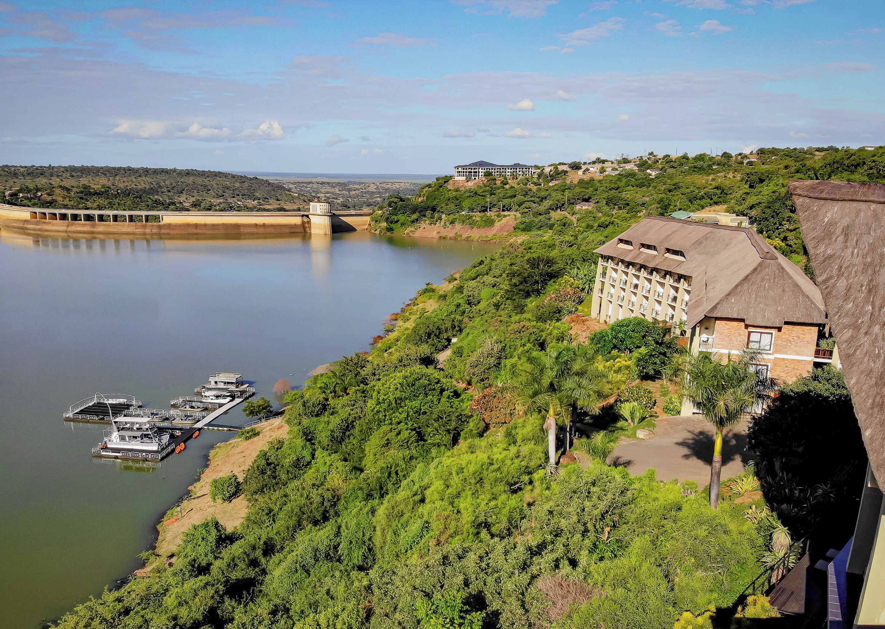 Un hôtel à toit de chaume, situé au bord d’une rivière où sont amarrés des bateaux.