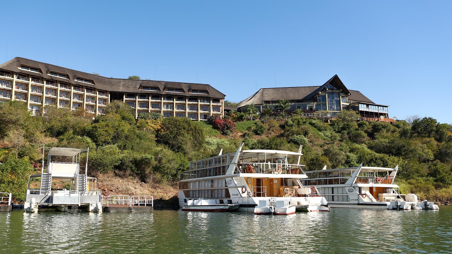 Une propriété située au bord de l’eau, avec plusieurs bateaux amarrés, un grand bâtiment doté de balcons et une végétation luxuriante.