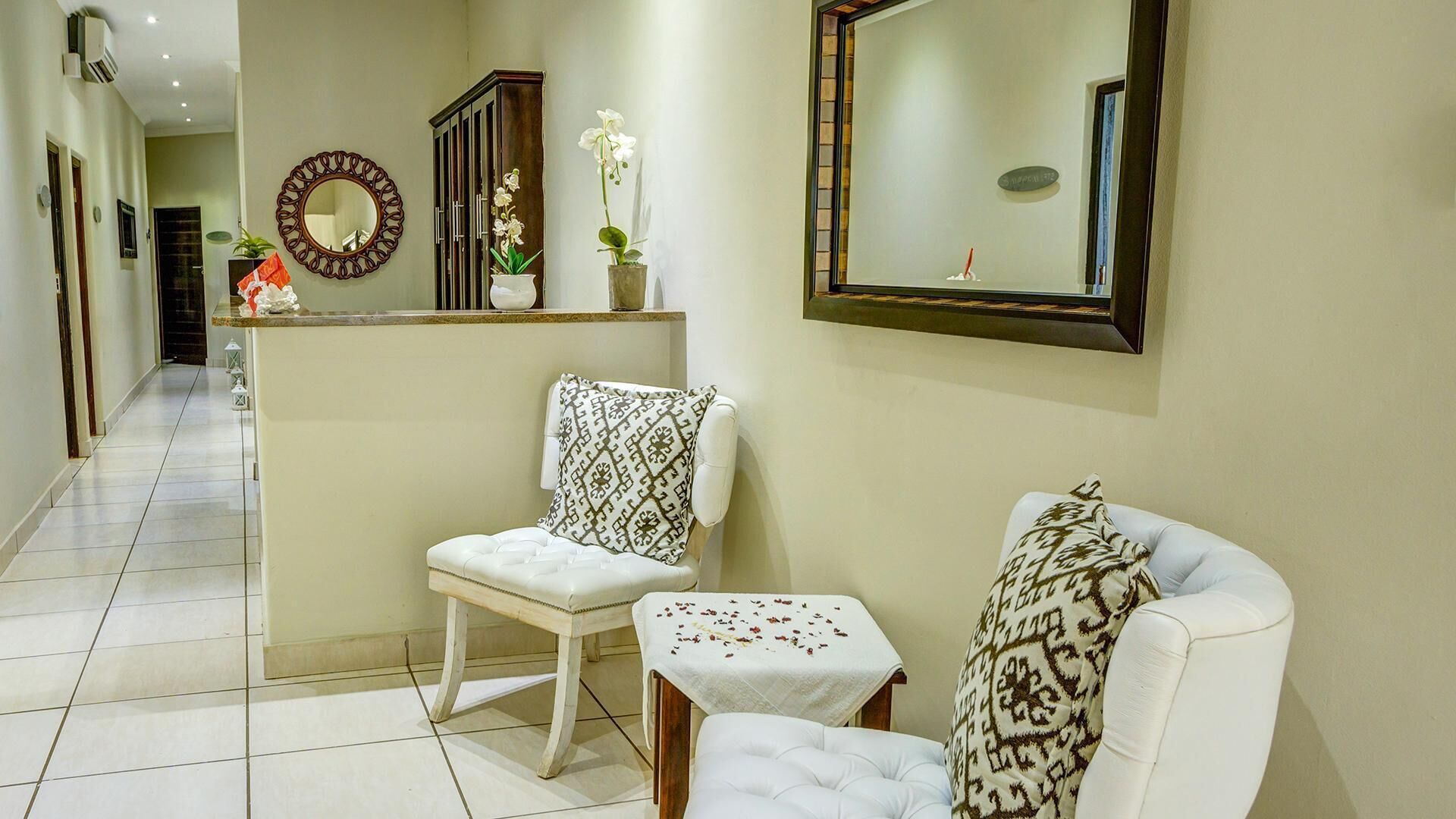 A hallway with a white chair, a small table, a mirror, and a cabinet with flowers.