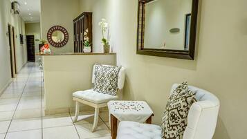 A hallway with a white chair, a small table, a mirror, and a cabinet with flowers.