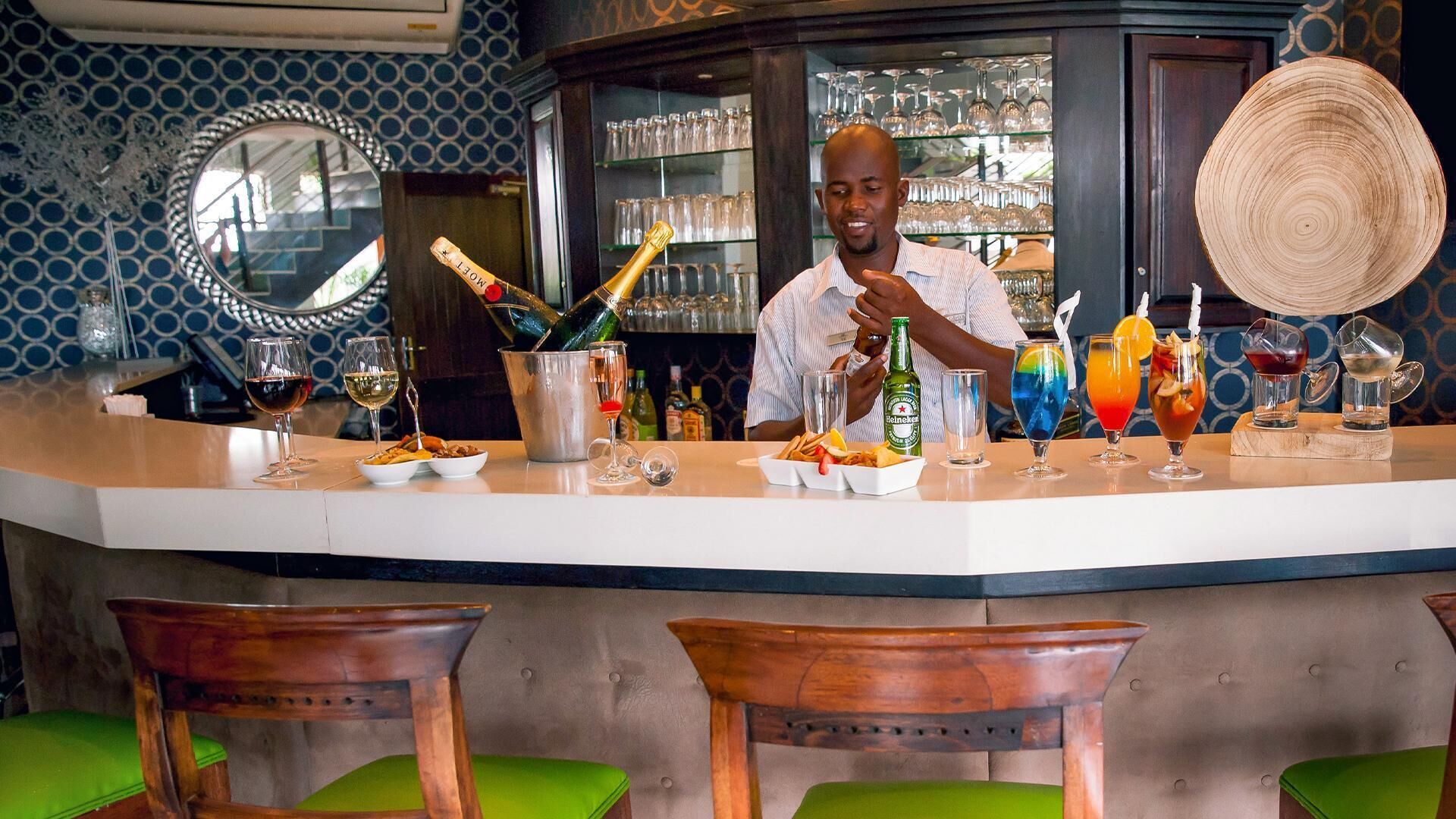 A bar area with a bartender, a variety of drinks, and a wine cooler.