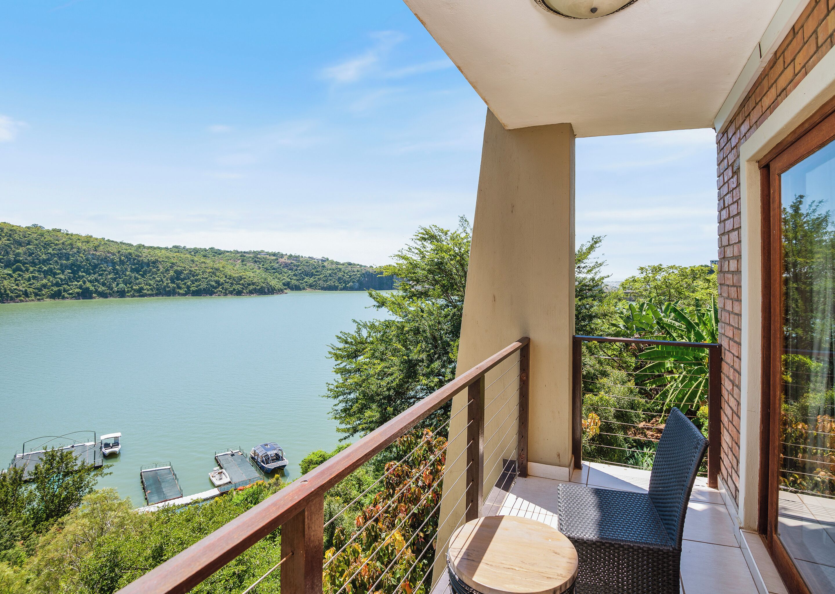 A balcony with a view of a lake, a boat dock, and lush greenery.