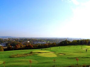 A golf course with well-maintained fairways and greens, surrounded by trees and a distant city skyline. - Le Green des Impressionnistes – Cergy‑Pontoise (Ennery)