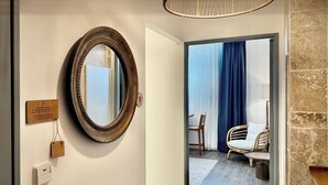 A hotel room with a wooden-framed mirror, a wooden plaque, a doorbell, and a view into a room with a chair and a table. - Le Green des Impressionnistes – Cergy‑Pontoise (Ennery)