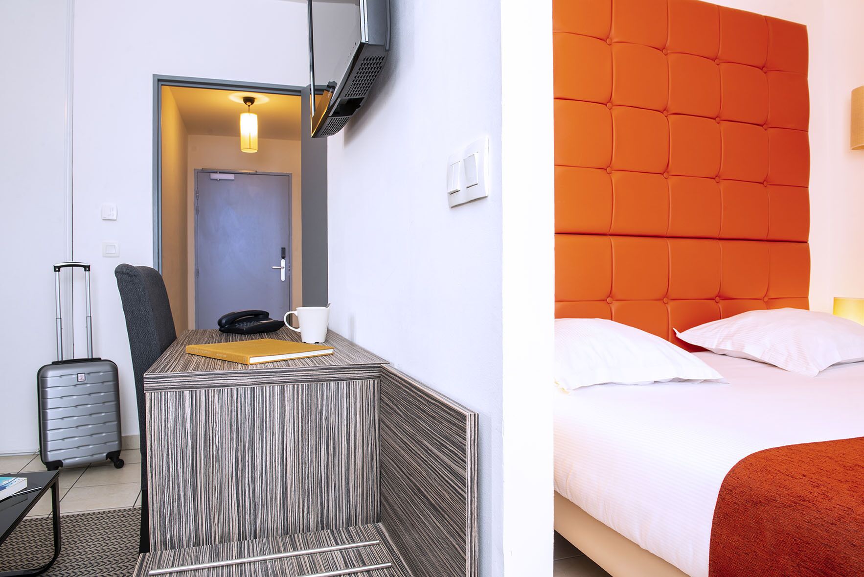 Una habitación de hotel con una cama, un escritorio con teléfono, una taza y una maleta.
