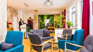 A hotel lobby with blue armchairs, a reception desk, and a green wall with plants. - Le Green des Impressionnistes – Cergy‑Pontoise (Ennery)