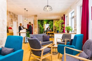 Un vestíbulo de hotel con sillones azules, una recepción y una pared verde con plantas.