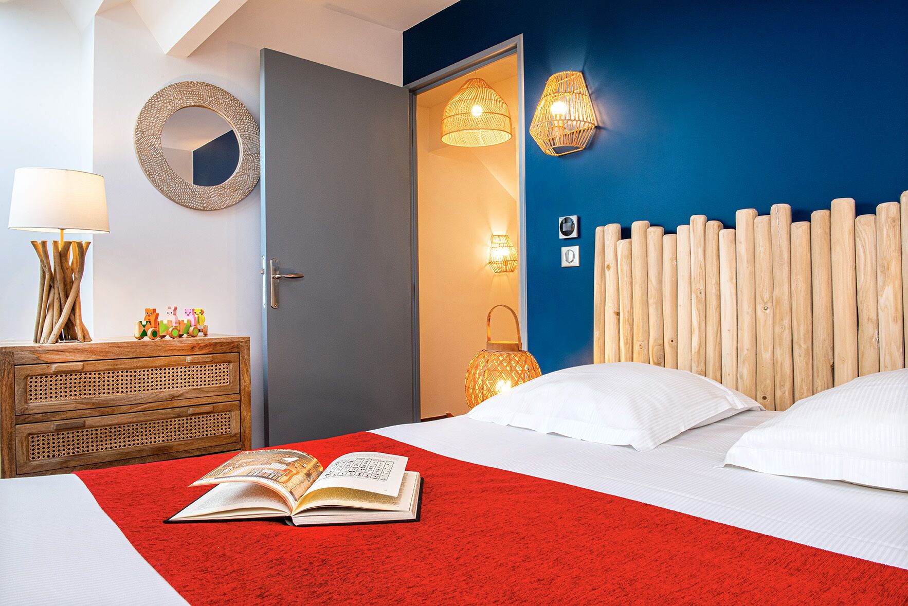 Un dormitorio con alfombra roja, cabecera de madera, mesita de noche con lámpara y puerta que da a otra habitación.
