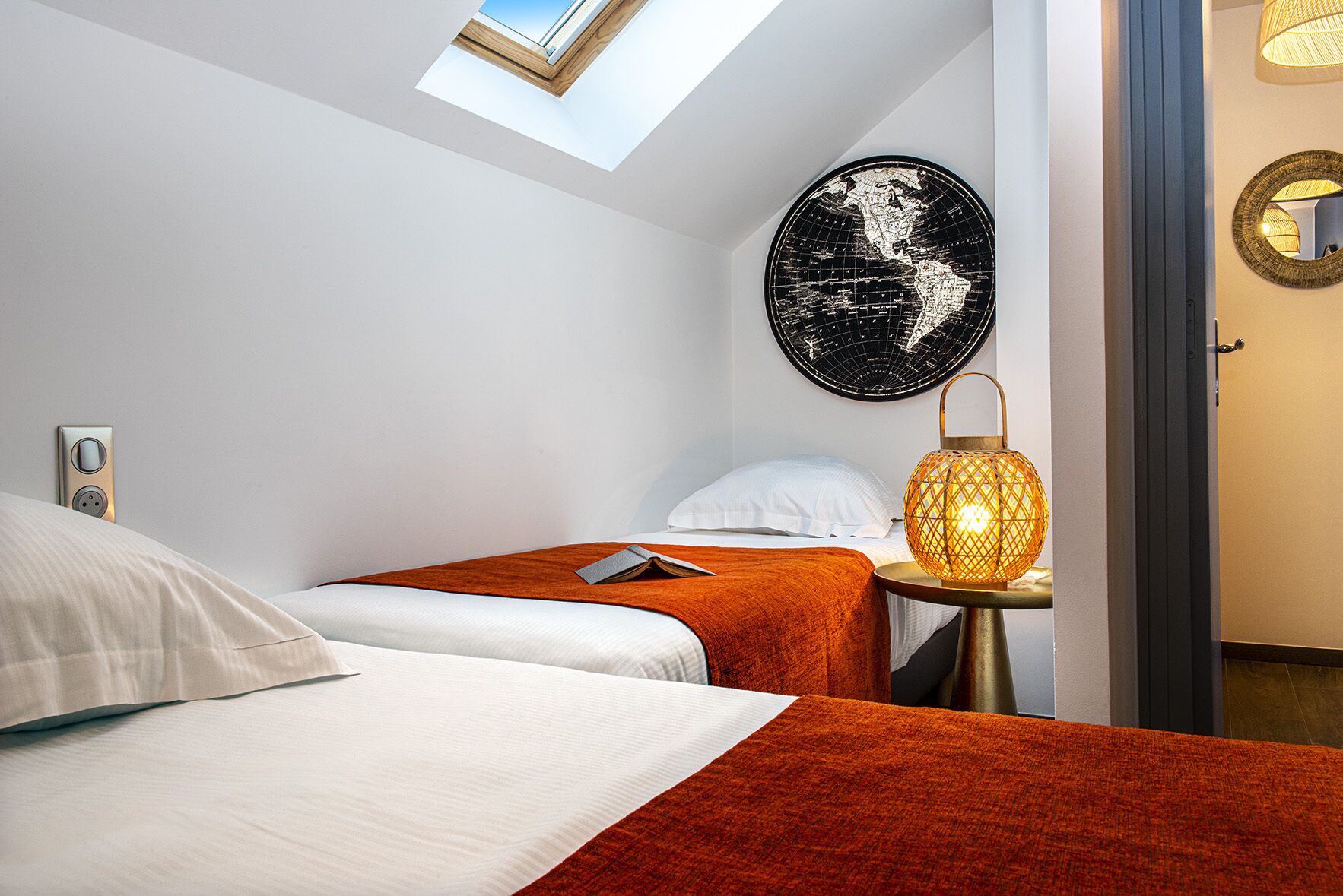Habitación de hotel con dos camas, un tragaluz, un mapa mural, una lámpara y un espejo.