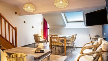 A cozy living room with a dining table, wicker chairs, a sofa, and a TV mounted on the wall.