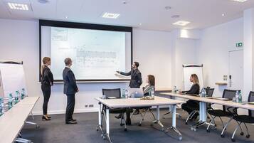 A conference room with a large projection screen displaying a presentation, a whiteboard, and a table with laptops and water bottles.