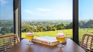Two glasses of beer on a table with a book and a view of a green landscape through large windows. - Le Green des Impressionnistes – Cergy‑Pontoise (Ennery)