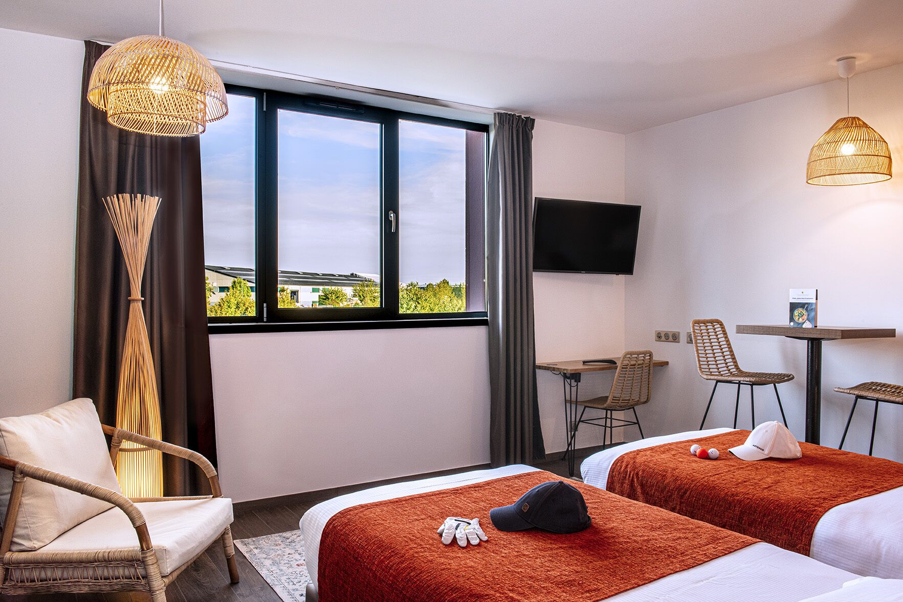 A hotel room with two beds, a desk, a TV, and a view of the outdoors.