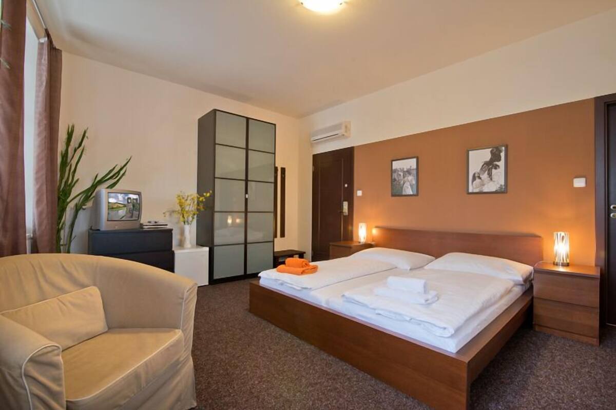 A hotel room with a bed, a sofa, a wardrobe, and a desk with a lamp.