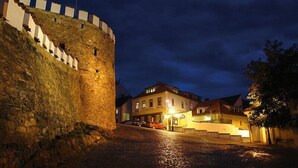 A stone fortification with a flag atop, adjacent to a building with multiple windows and a sign. - U Zlateho byka (Pisek)