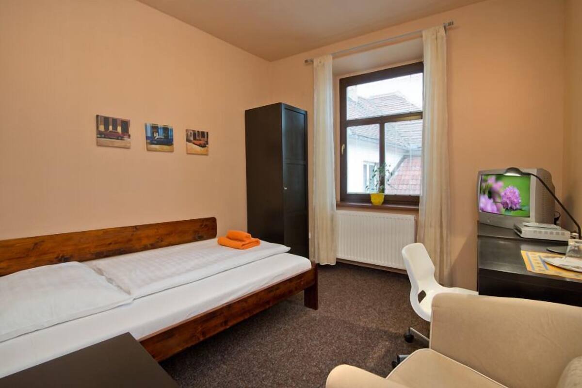 A bedroom with a single bed, a wardrobe, a desk with a computer, a chair, and a window with curtains.
