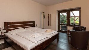 A double bed with white linens, a wooden headboard, a bedside table with a lamp, and a view of greenery through a window. - U Zlateho byka (Pisek)