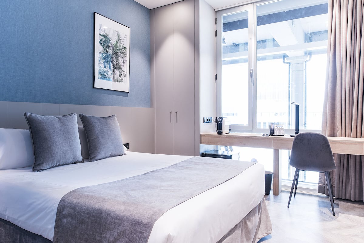 A modern hotel room with a bed, bedside table, and a desk with a chair.