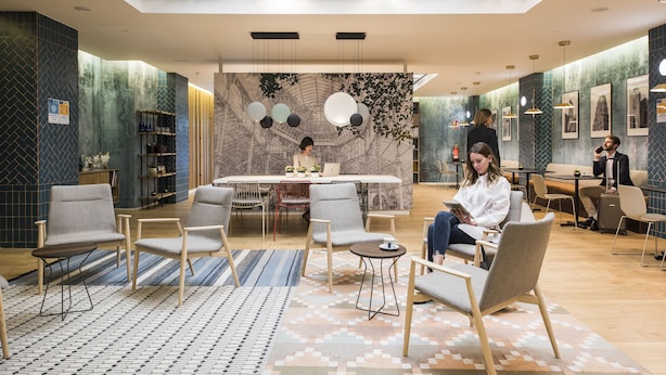 Een moderne hotellobby met een centrale zithoek, een receptiebalie en een muurschildering op de achterwand.