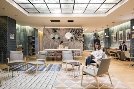 A modern hotel lobby with a central seating area, a reception desk, and a mural on the back wall.