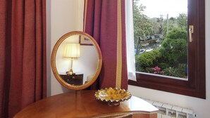 A wooden bedside table with a round mirror, a lamp, and a decorative bowl. - Villa Dacri (Venice)