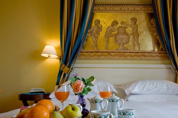 Une chambre d’hôtel avec un lit, une table garnie de fruits, un vase avec une rose et un tableau accroché au mur.