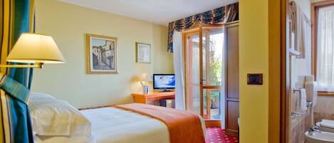 Habitación de hotel con cama, escritorio con computadora, televisión y baño visible a través de una puerta abierta.