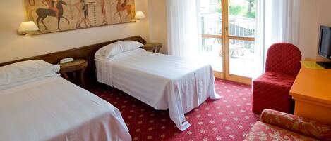 Habitación de hotel con dos camas individuales, un sillón rojo, un televisor y un mural en la pared.