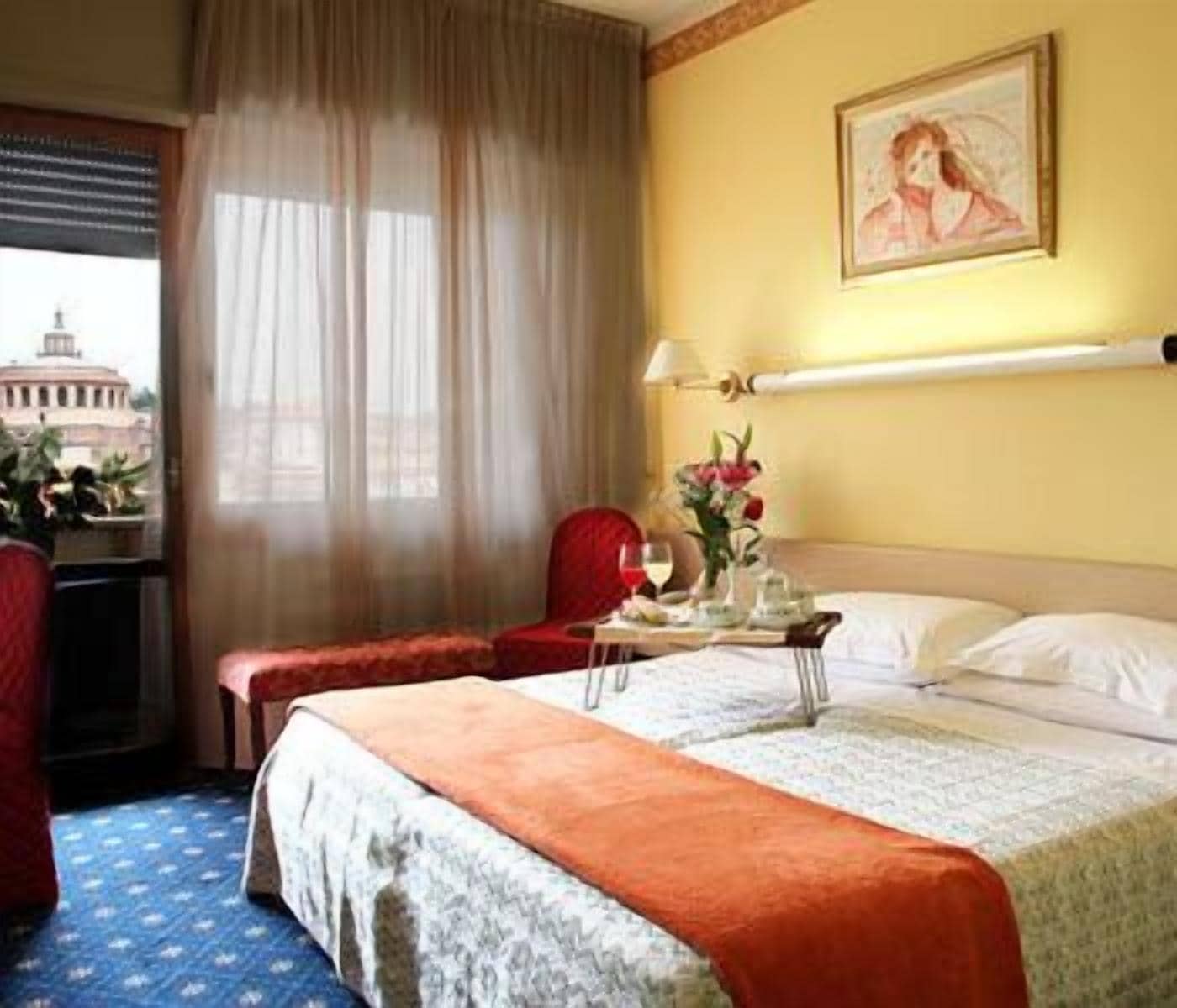 Une chambre d’hôtel avec un lit, une chaise, une table ornée d’un vase de fleurs et un tableau accroché au mur.