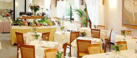 A restaurant with multiple tables and chairs, each set with a white tablecloth and a vase of flowers.