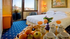 Habitación de hotel con cama, bandeja de desayuno con frutas y pasteles, un florero con flores y un cuadro en la pared.
