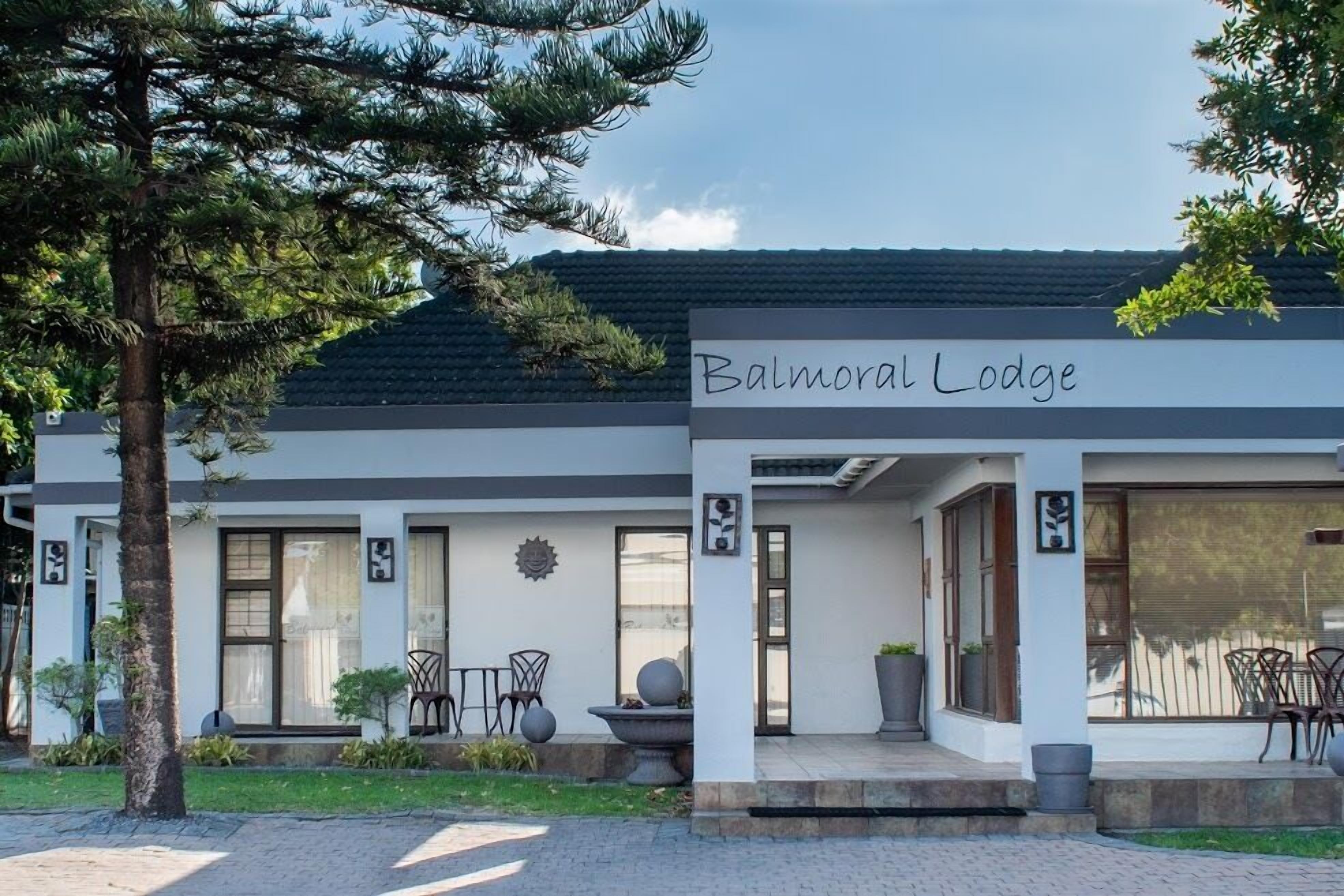 Un edificio llamado "Balmoral Lodge" con un diseño moderno, que cuenta con amplios ventanales, asientos al aire libre y un jardín bien cuidado.