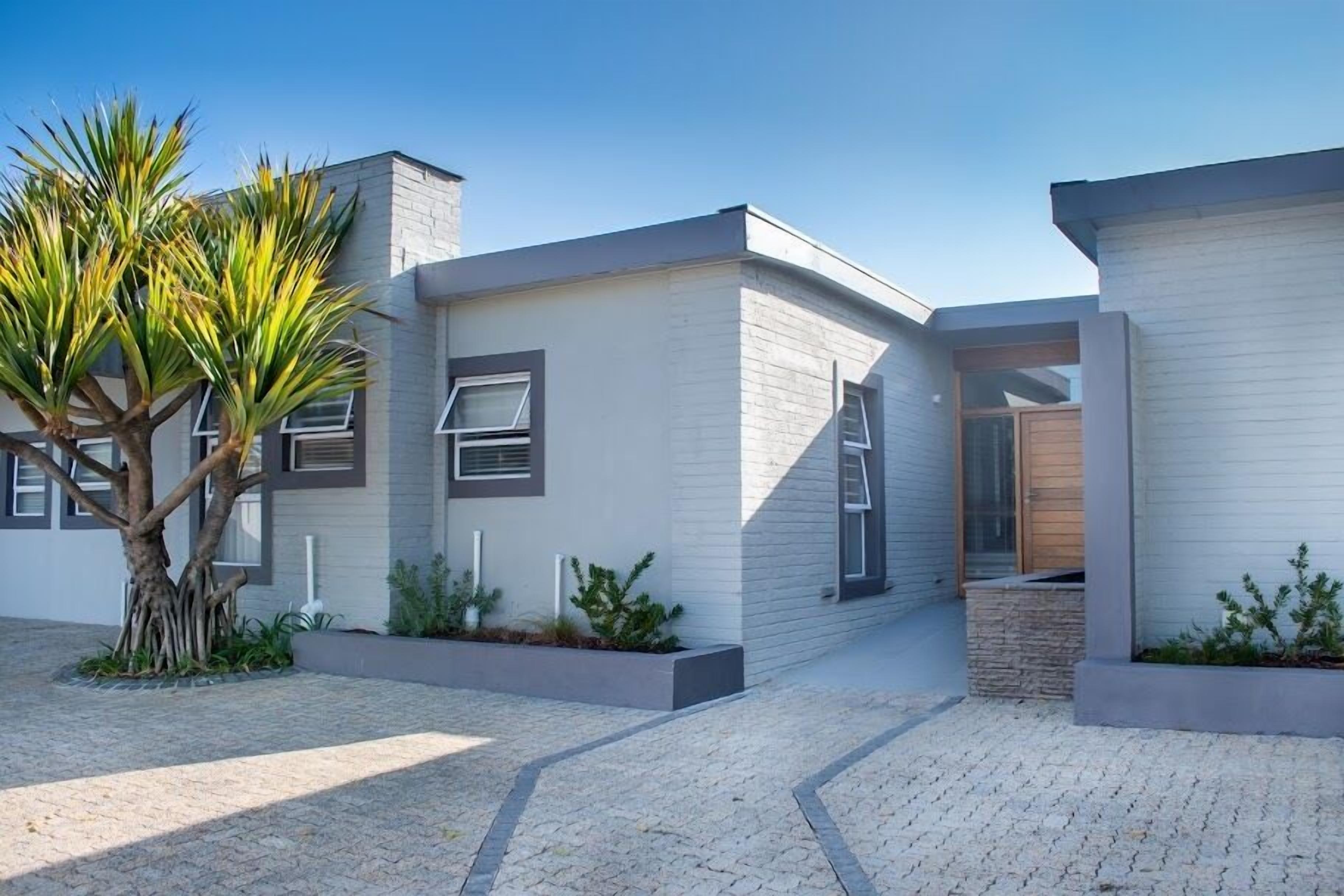 A modern house with a paved driveway, a large tree, and a small garden area.