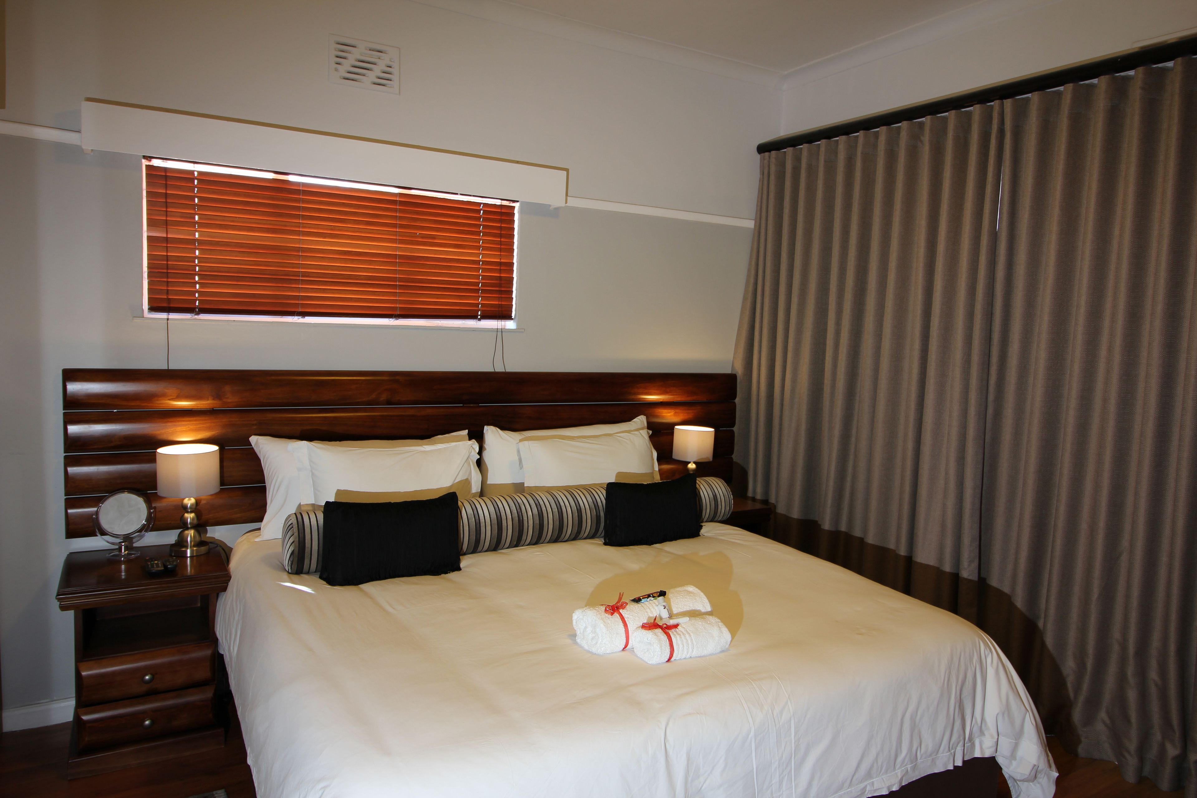 Habitación de hotel con una cama grande, dos mesitas de noche, una ventana con persianas y una cortina.