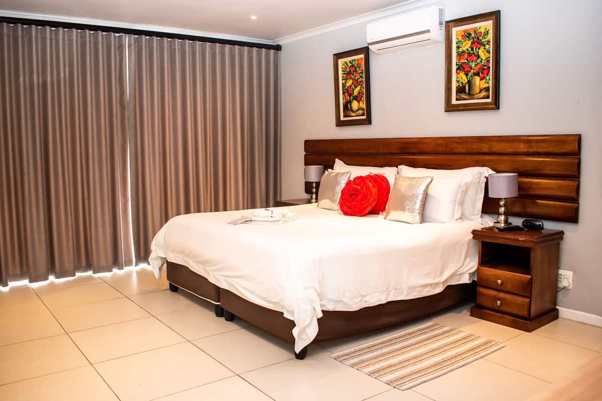 Quarto de hotel com uma cama grande, uma mesa de cabeceira, dois aparelhos de ar condicionado na parede e uma janela com cortinas.