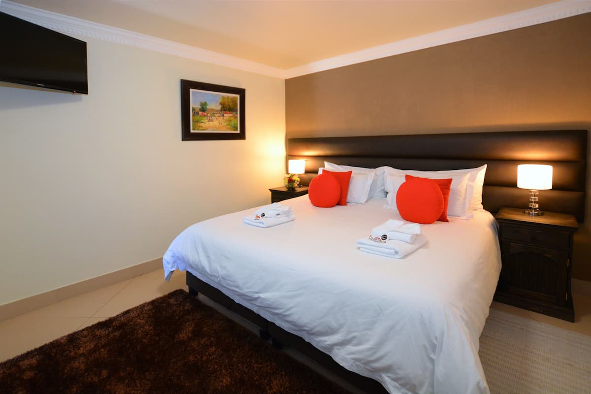 Cama bem arrumada com lençóis brancos e almofadas vermelhas, uma cabeceira escura e um quadro na parede.